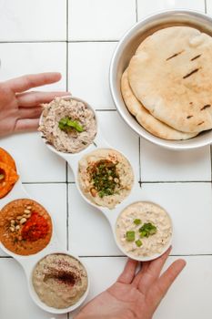 Colorful assortment of Middle Eastern dips with pita bread on a white tiled surface.