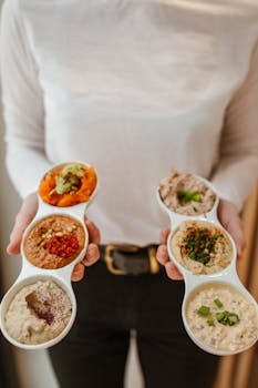 Person holding a selection of flavorful dips, showcasing diverse Middle Eastern cuisine.