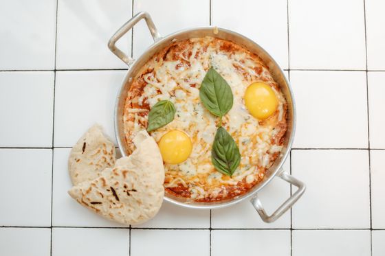 Pan of eggs baked in tomato sauce under melted cheese with basil leaves and flatbread