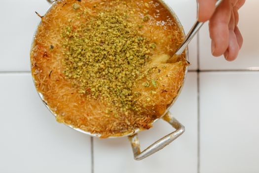Close-up of knafeh topped with pistachios, a hand holding a spoon.