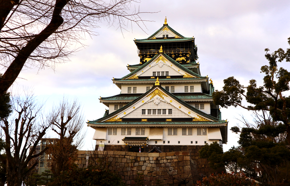 Majestic view of Osaka Castle surrounded by bare trees under a cloudy sky during winter.