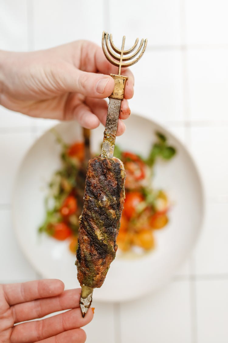 A Person's Hands Holding A Skewer With Grilled Meat