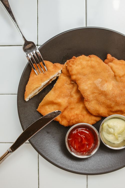 Free Crispy schnitzel served with ketchup and mayonnaise on a black plate. Stock Photo