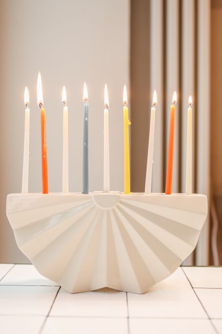 A ceramic menorah with colorful candles lit for Hanukkah celebration indoors.