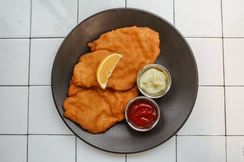 Free Golden fried schnitzel served with lemon, ketchup, and mayo on a ceramic plate. Stock Photo