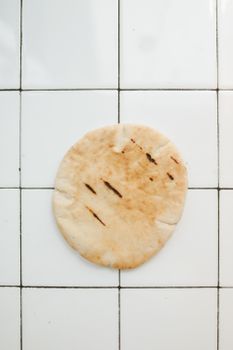 A freshly baked pita bread resting on a clean white tiled surface, perfect for food and bakery themes.