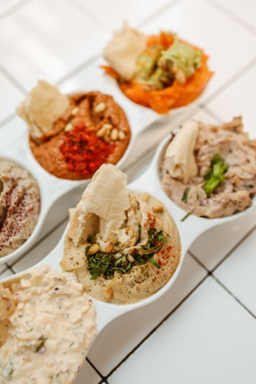 Free Assorted hummus dips with toppings displayed on a white tiled surface. Stock Photo