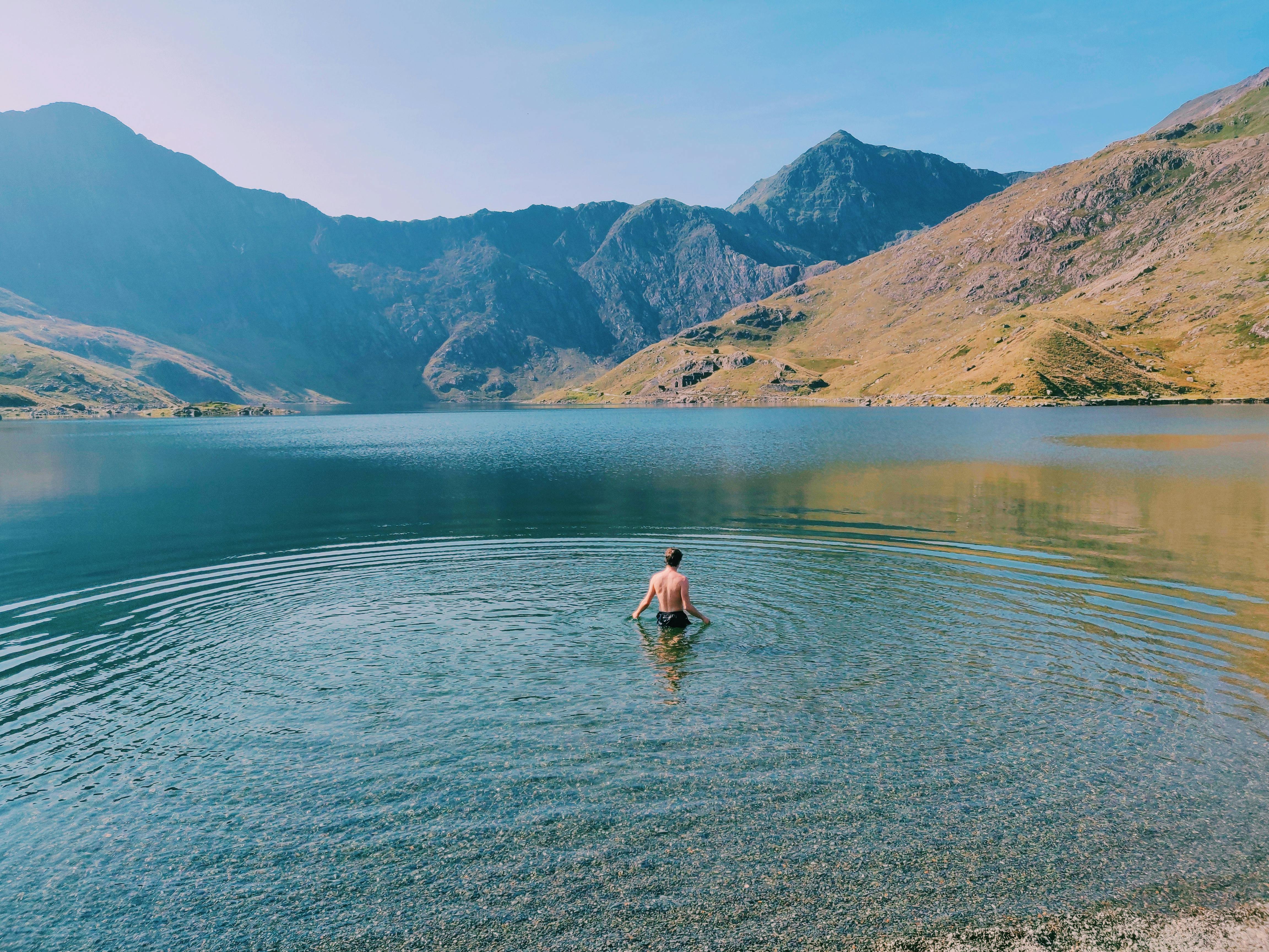 A man swimming in a tranquil lake in Wales, surrounded by scenic mountain views at sunrise.