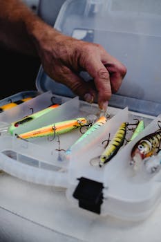 Hand selecting fishing lures from an organized tackle box, perfect for fishing enthusiasts.