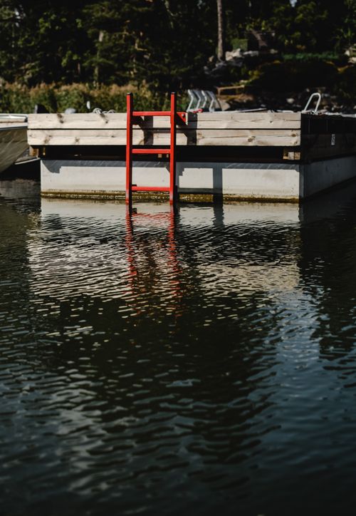 Free A quiet lakeside view featuring a red ladder on a dock, reflecting in the calm waters of Finland. Stock Photo