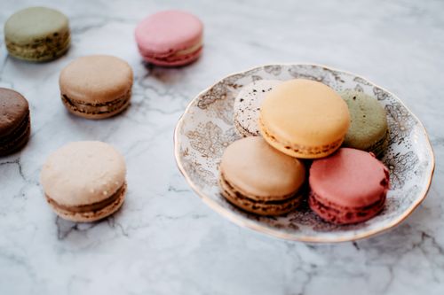 Free A close-up of colorful macarons on a decorative porcelain plate with a marble backdrop. Stock Photo
