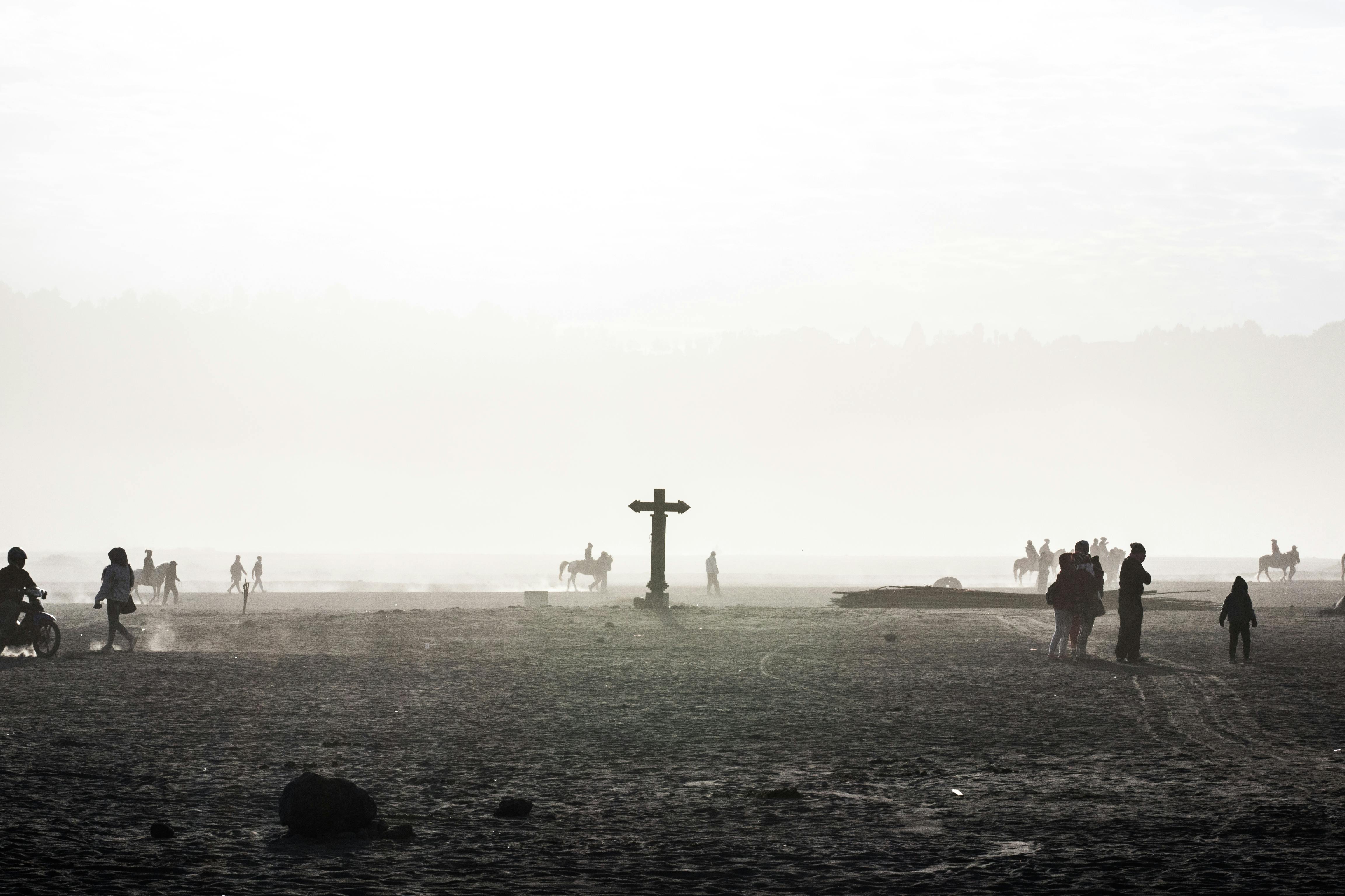Silhouetted people and horses in the misty sands of Bromo, East Java at sunrise.