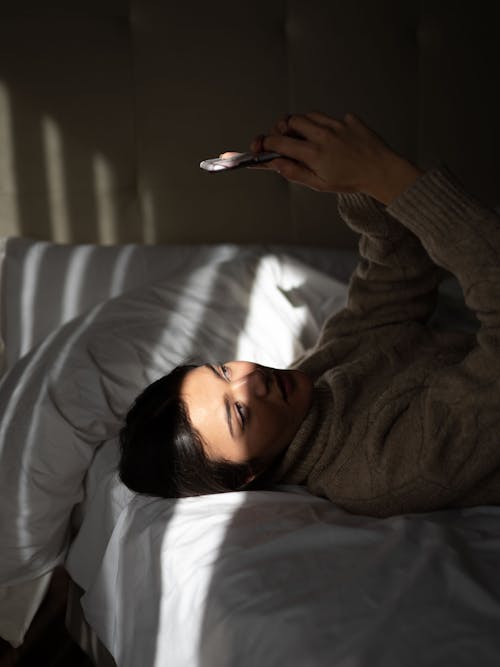 Relaxed young lady lying on bed and using smartphone