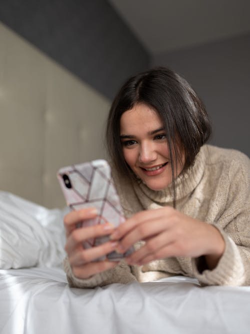 Free Positive young female messaging on smartphone in bedroom Stock Photo