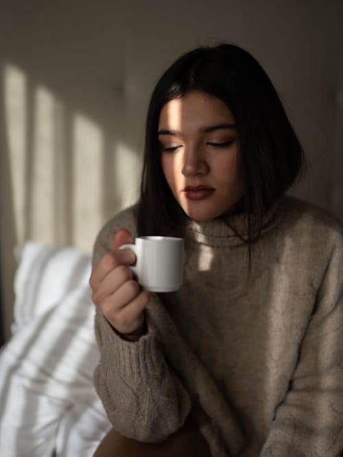 Free Dreamy young woman drinking coffee on bed Stock Photo