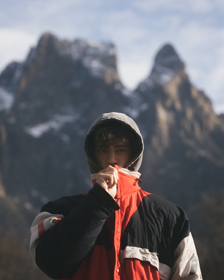 Serious Young Male Hiker Standing Near Snowy Mountains In Sunlight