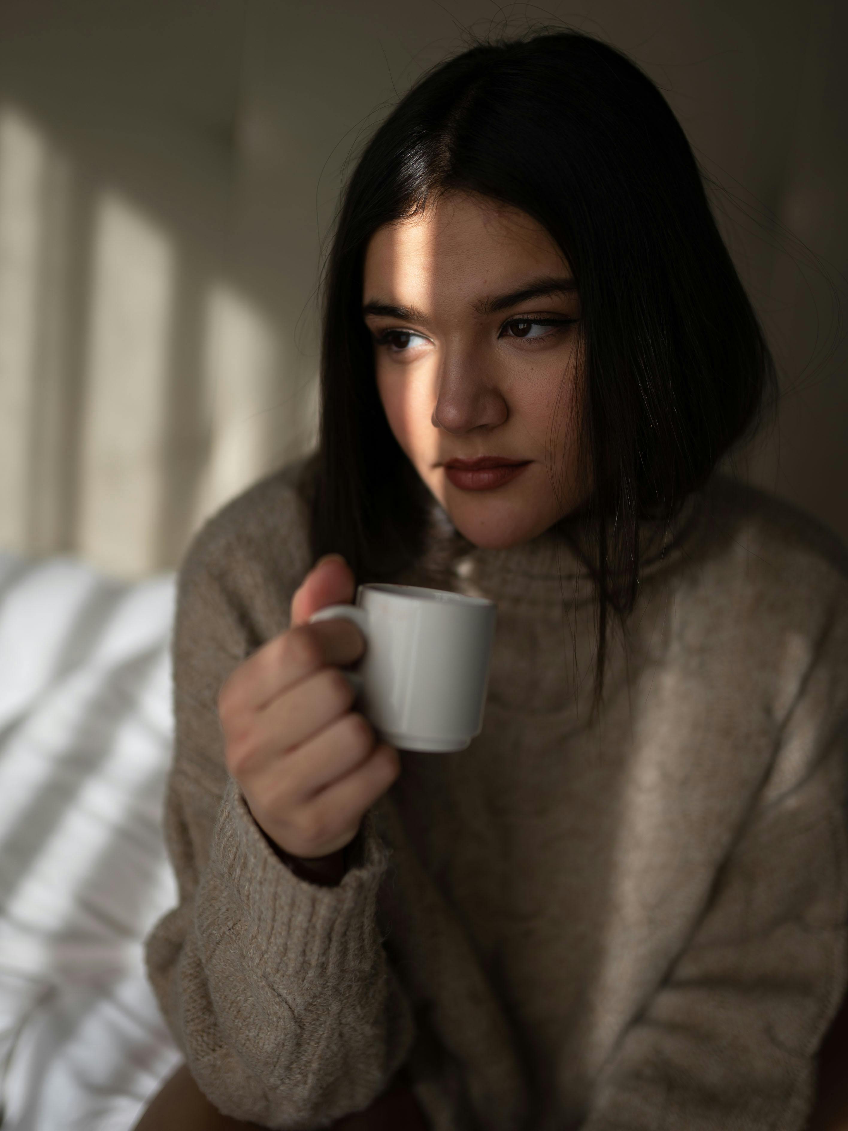 Thoughtful young woman drinking coffee near window on gloomy day · Free ...