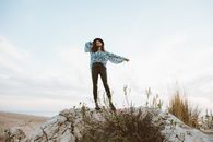 Woman in Blue and White Floral Shirt and Black Pants Standing on Rock Formation