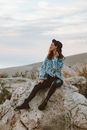 Woman in Blue and White Floral Shirt and Black Denim Jeans Sitting on Rock