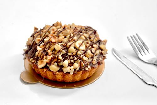Free Appetizing sweet pie tart with shortcrust pastry and chopped nuts topped with chocolate sauce on white background near fork and knife Stock Photo
