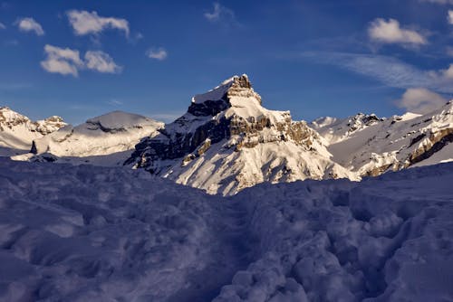 Majestic mountain range covered with hoarfrost located among snowy terrain against cloudy sky on winter day in sunny nature