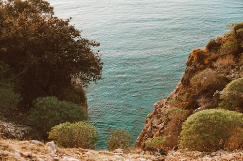 Free Breathtaking view of a rocky cliff with lush vegetation meeting the turquoise ocean waters, perfect for nature lovers. Stock Photo