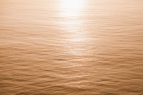 Free Serene aerial view of the ocean with golden sunset reflections creating a tranquil scene. Stock Photo