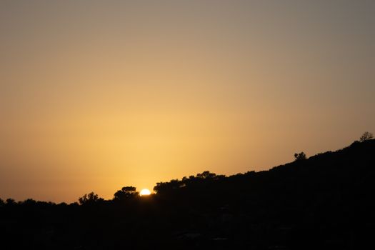 A tranquil sunset over silhouetted rolling hills, capturing nature's golden hour glow.