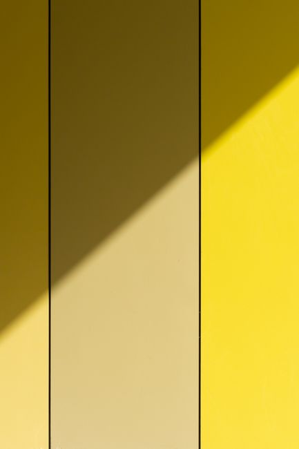Minimalist yellow wall with geometric shadow play creating an abstract visual.