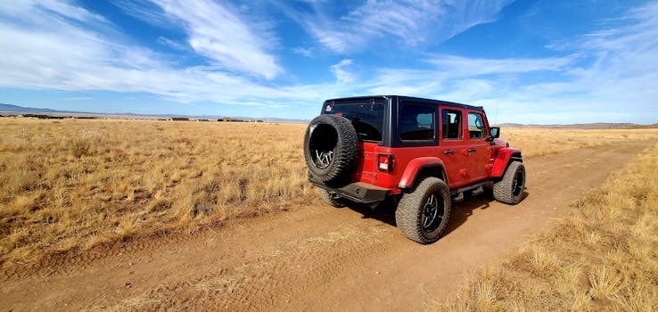 A red SUV on a dirt road amidst the expansive Arizona desert under a blue sky.