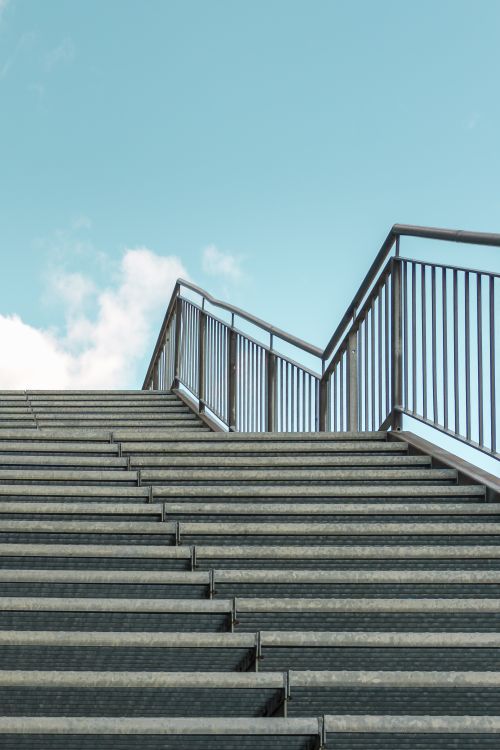 Free A modern metal staircase leading upwards against a clear blue sky, perfect for industrial themes. Stock Photo