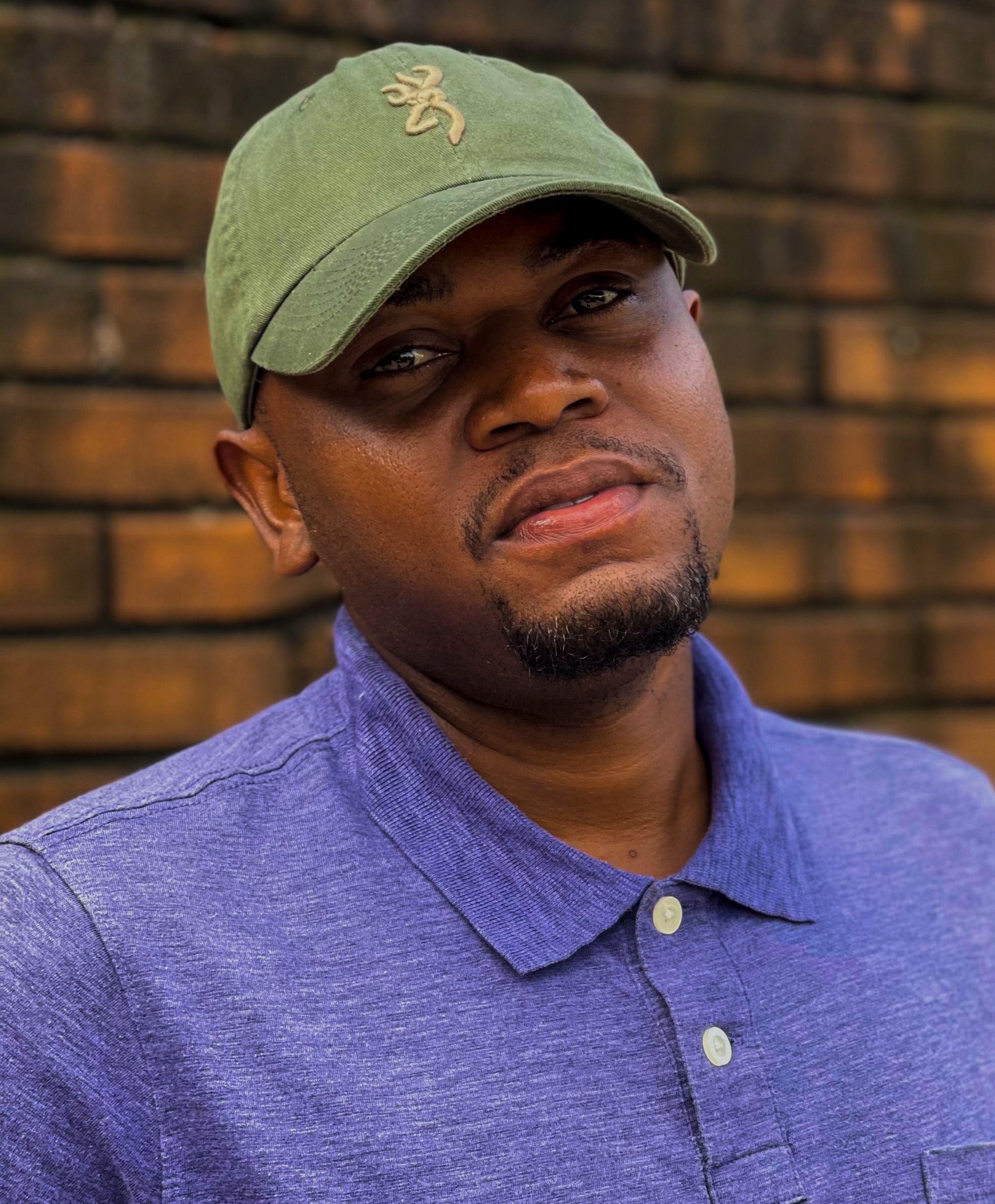 Portrait of a man wearing a green cap and blue polo shirt outdoors.