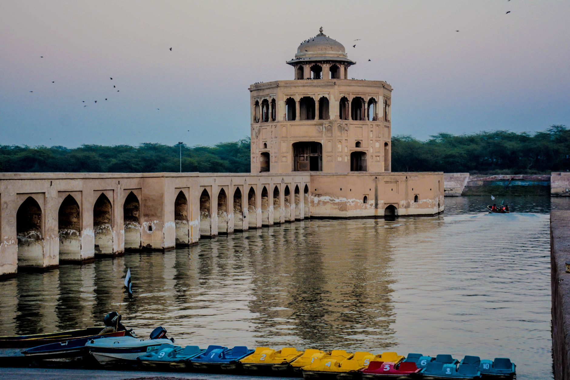 Serene view of Hiran Minar pavilion with boats at sunset in Sheikhupura, Pakistan.
