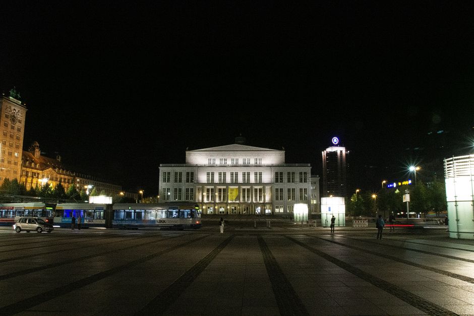 A nighttime view of the illuminated Leipzig Opera House with surrounding cityscape.