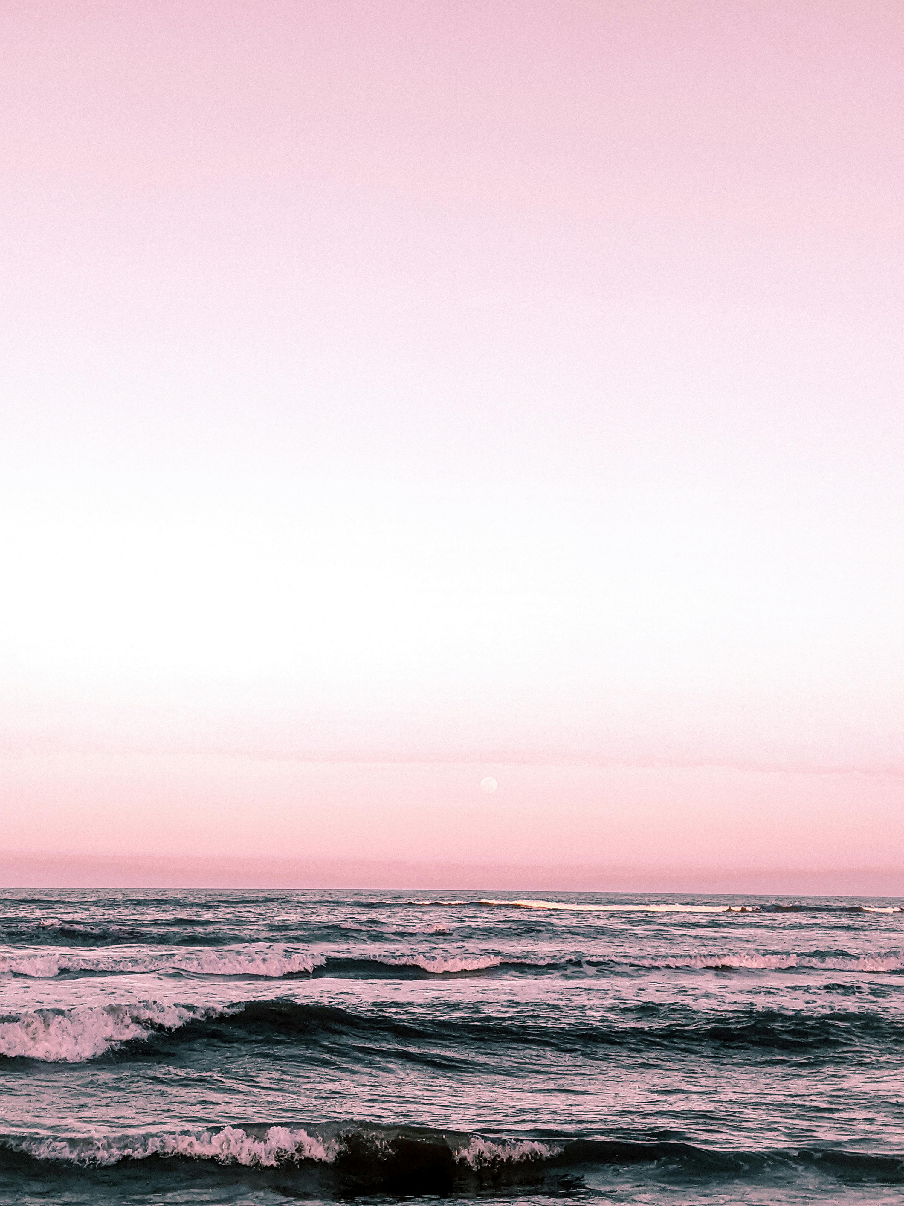 A tranquil seascape with crashing waves under a pink twilight sky, offering a serene coastal view.