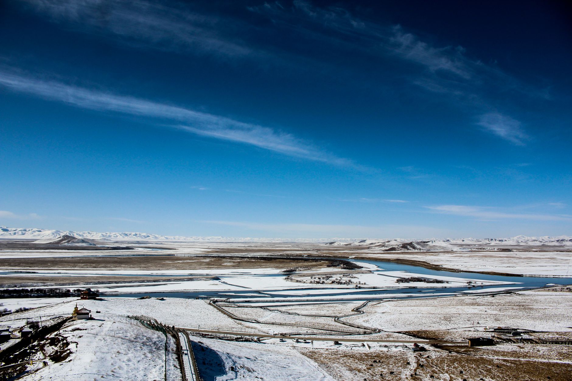 Expansive snowy landscape with rivers and distant mountains in West Sichuan, China.