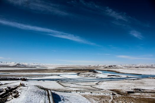 Expansive snowy landscape with rivers and distant mountains in West Sichuan, China.