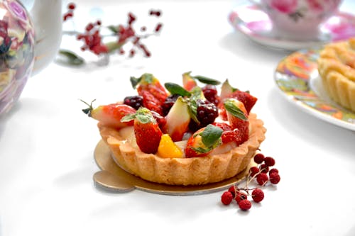 Tasty tarlet decorated with ripe strawberries on table with fresh berries near tea set on blurred background in light kitchen