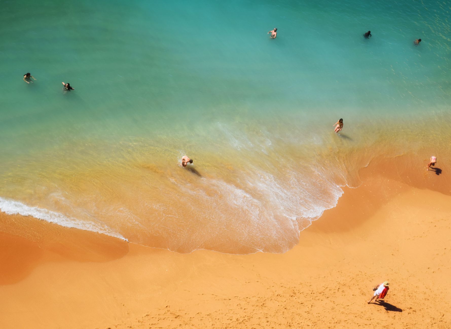 A scenic aerial view of people swimming and relaxing on a sandy beach under the sun.