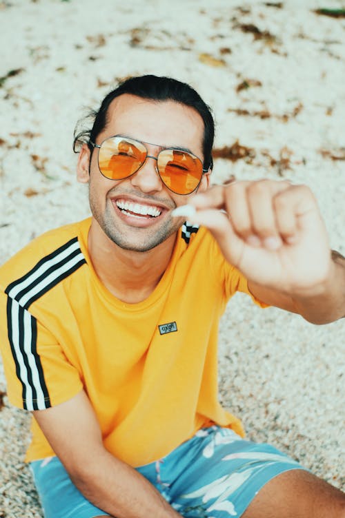 From above of positive male smiling and looking at camera while demonstrating little stone on blurred background of beach