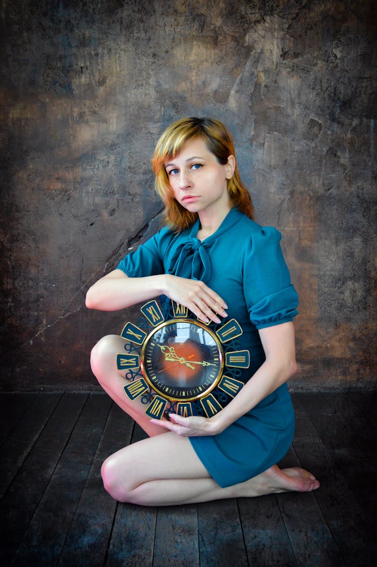 Unemotional Woman Sitting On Floor With Round Clock In Hands