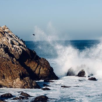 Powerful ocean waves crashing against rocky coastline under clear sky. Dynamic seascape highlighting natural beauty.