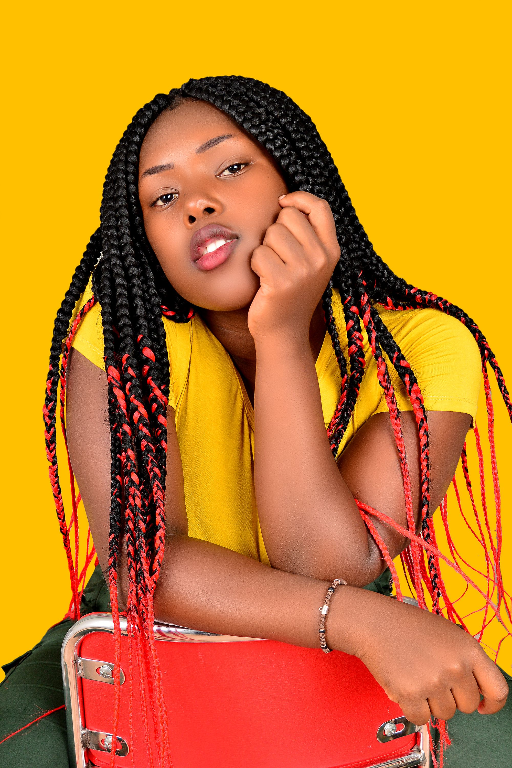 A vibrant studio portrait of a young woman with braided hair against a yellow background, exuding style and confidence.