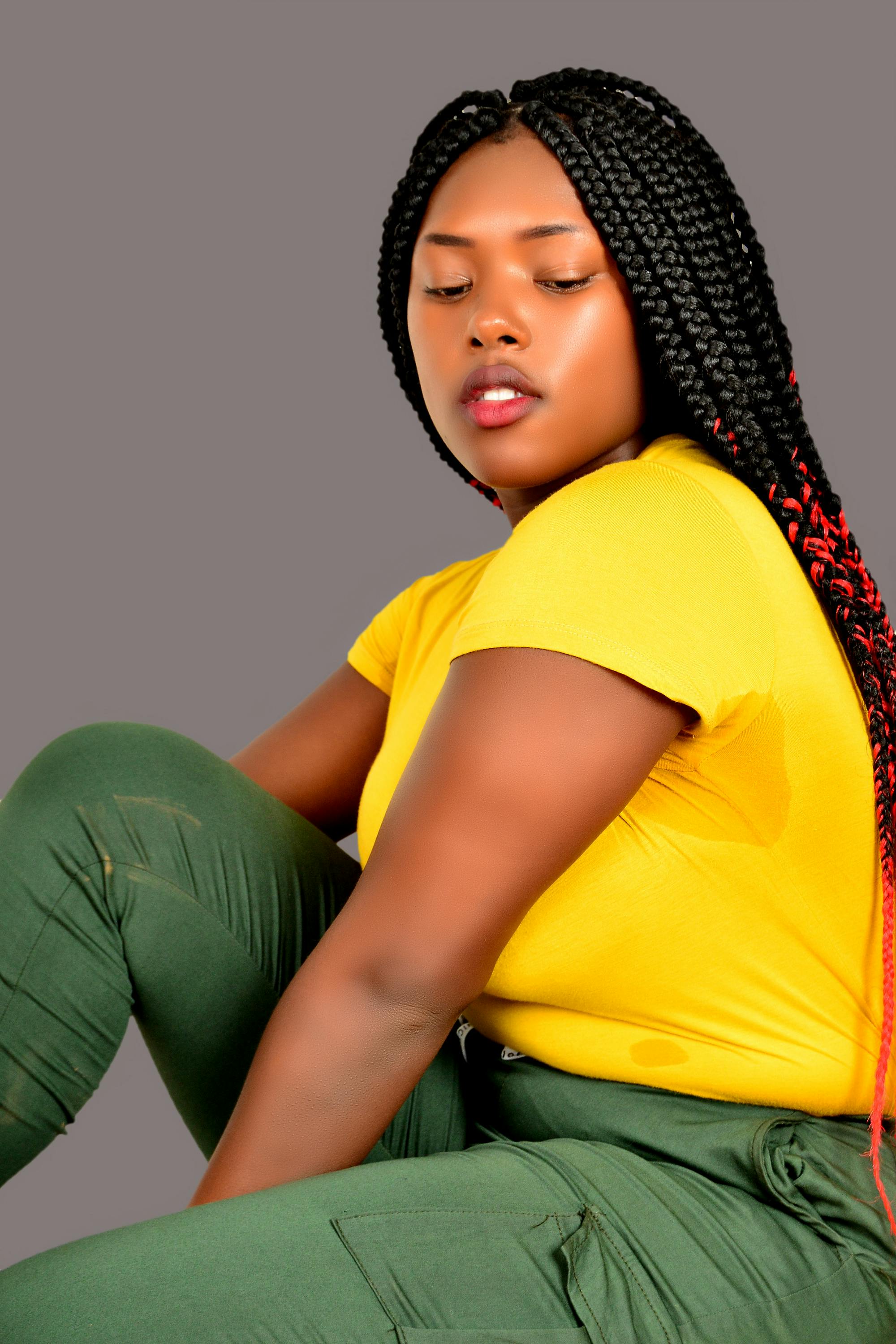 Portrait of a model with braids posing in a studio with a vivid yellow outfit.