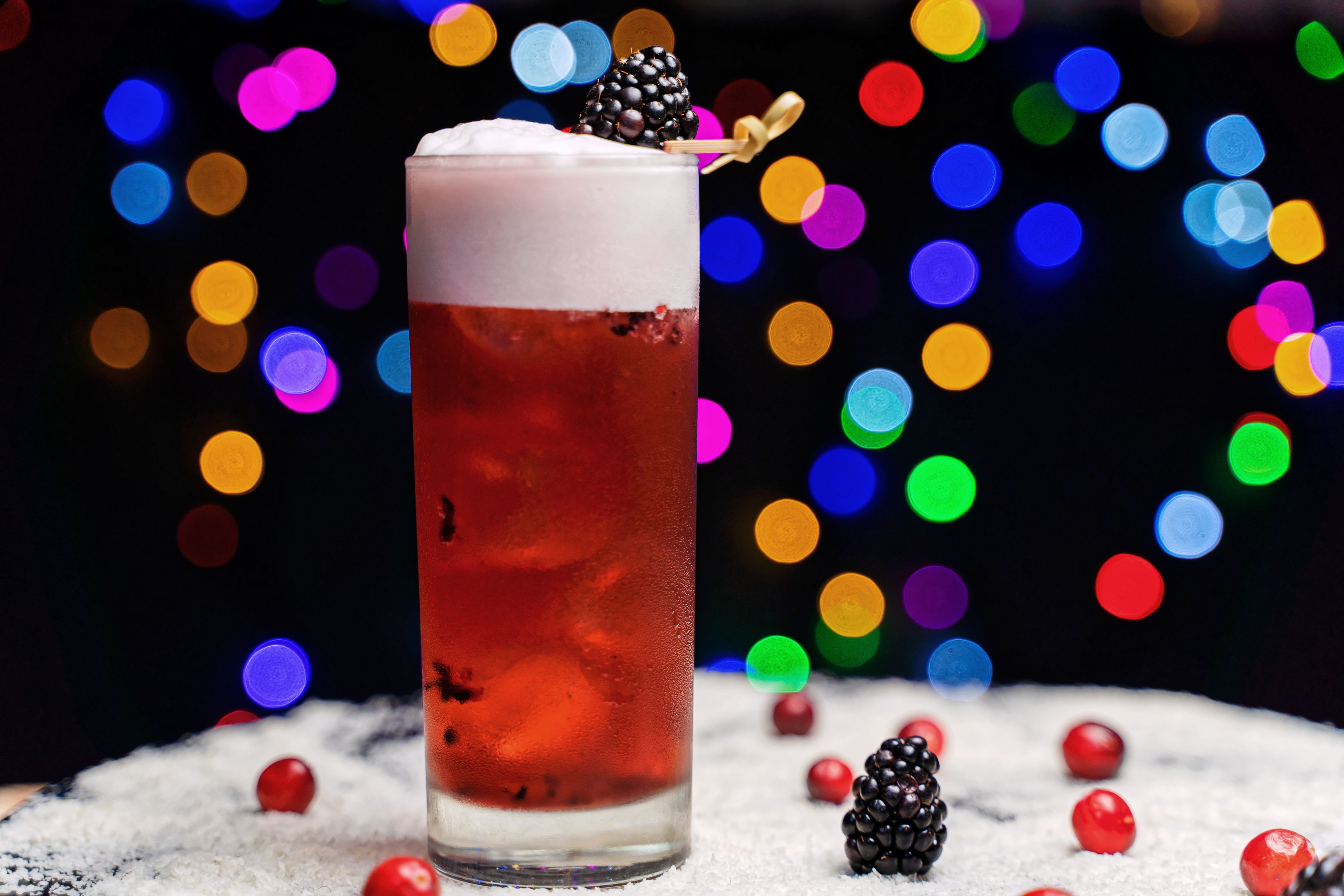 Vibrant red mocktail with berries and festive bokeh background, perfect for celebrations.