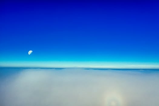 A breathtaking aerial view showcasing the blue sky, clouds, and visible moon at daytime.