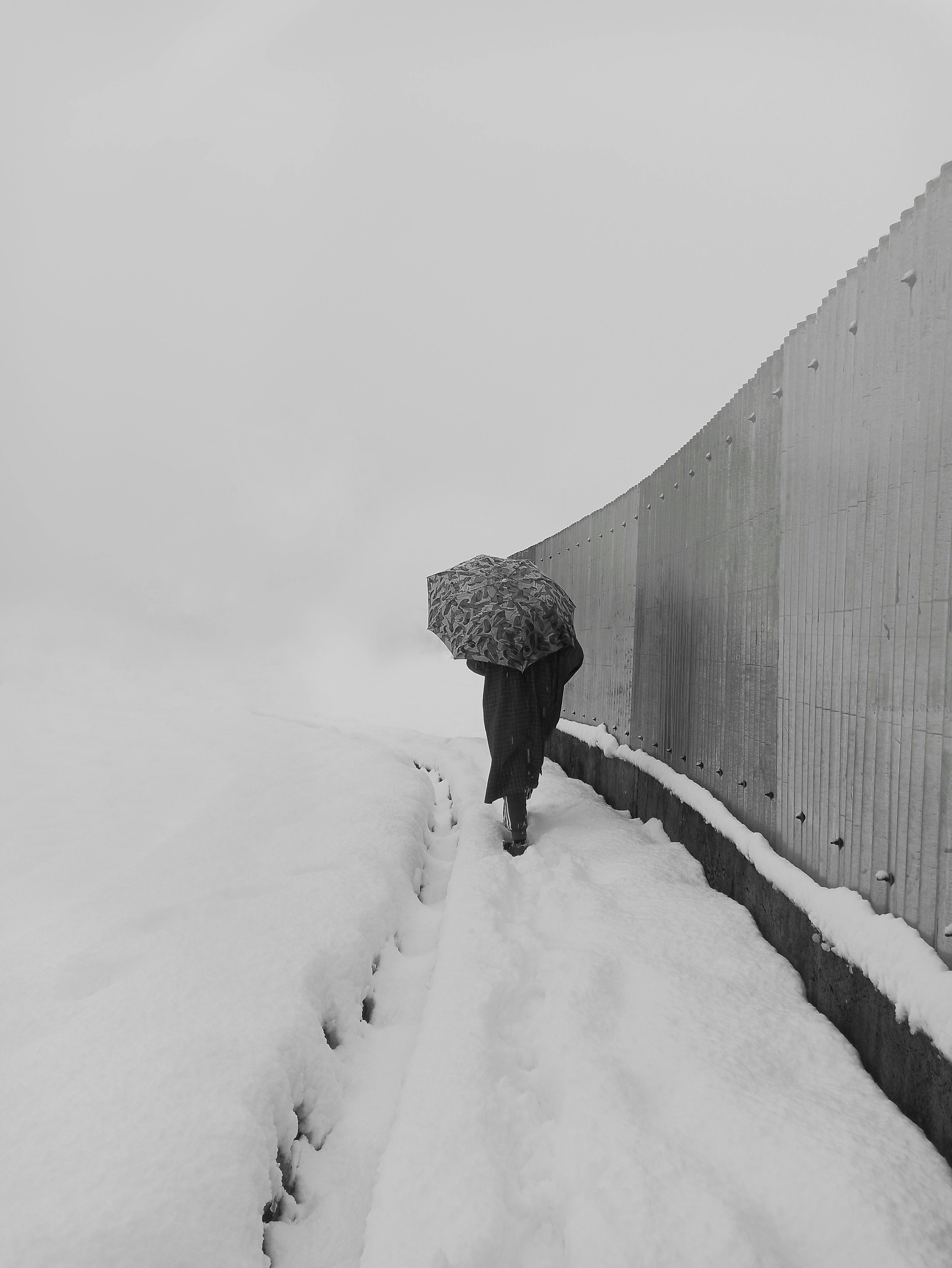 person in black coat walking on snow covered pathway