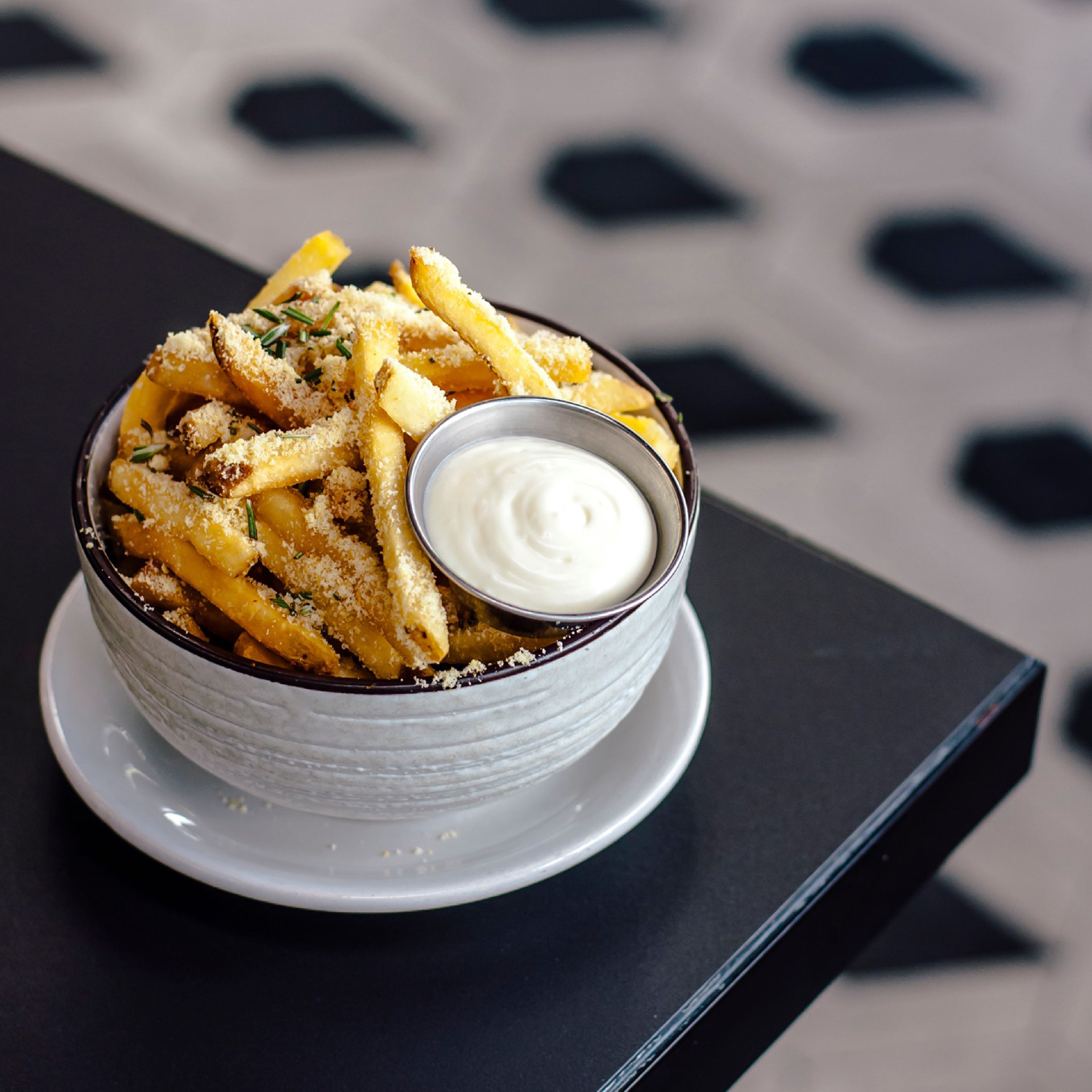 A bowl of crispy French fries topped with parmesan and herbs served with creamy dip.