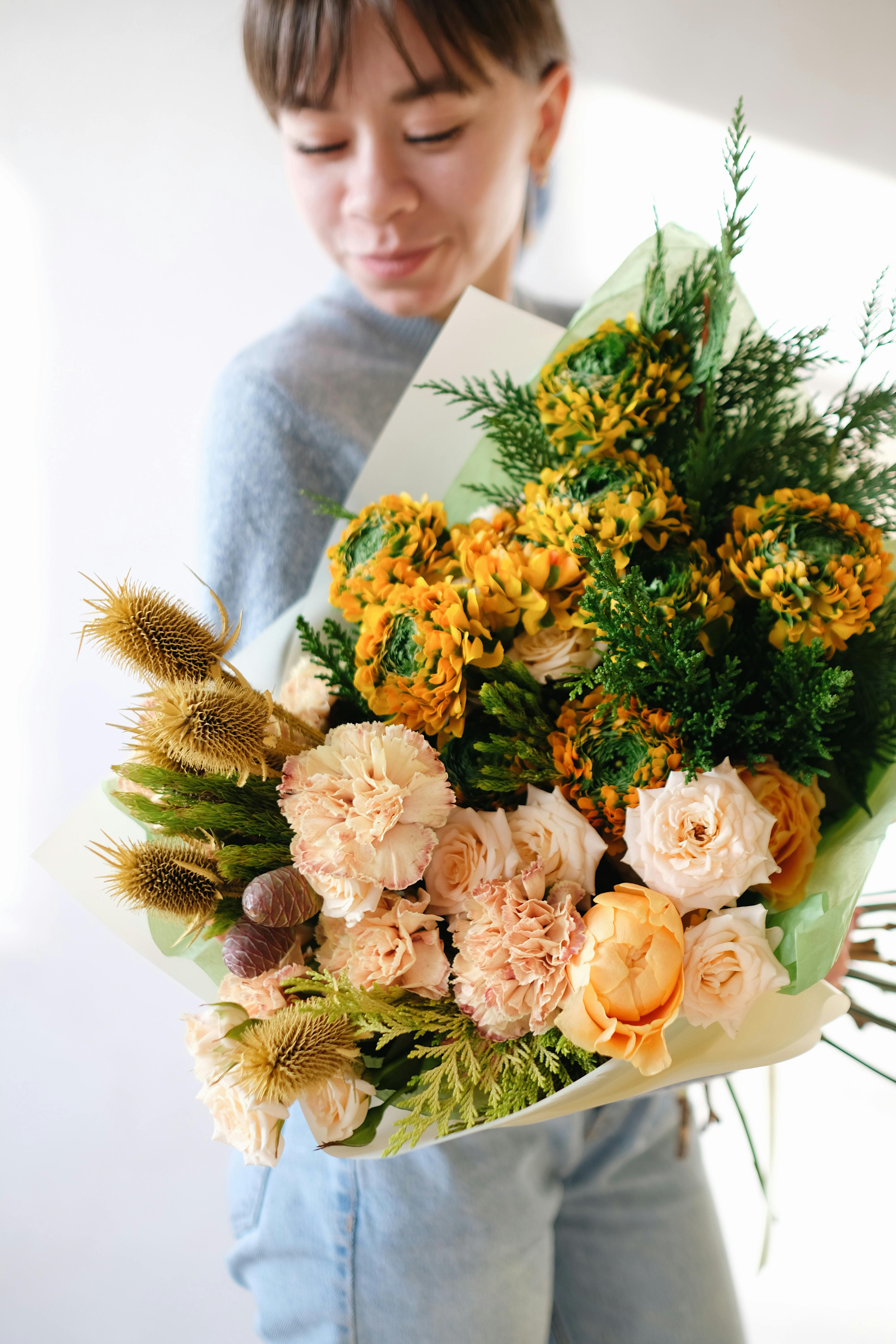 A smiling woman holds a vibrant floral bouquet with yellow and pink flowers.