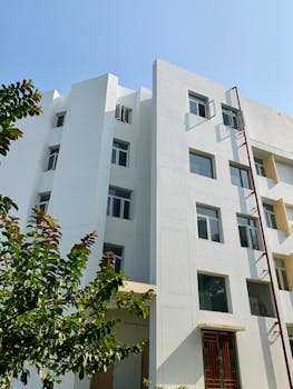 Contemporary white apartment building facade with glass windows and leafy foreground.